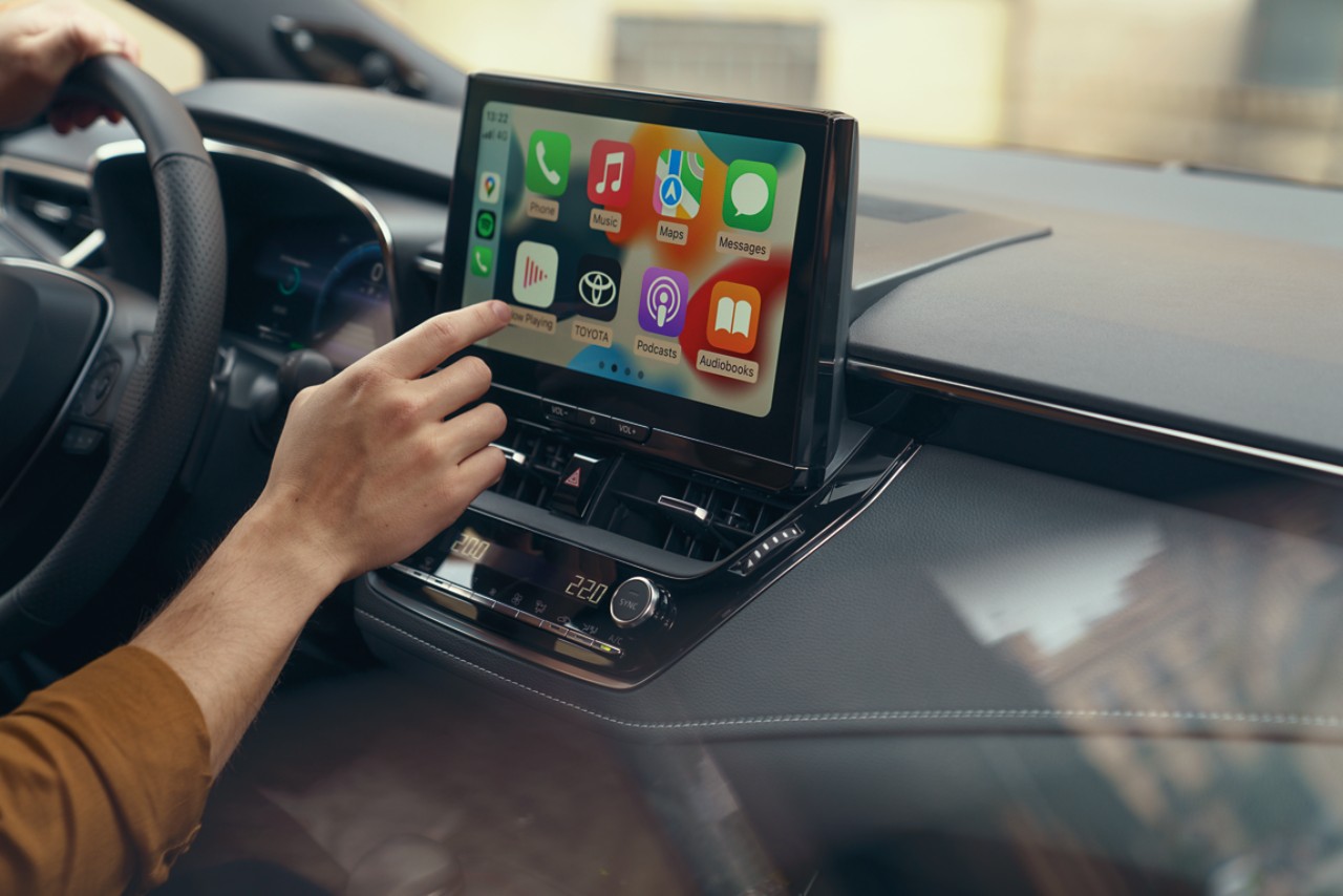 Osoba vo vozidle Toyota používa multimediálnu dotykovou obrazovkou vozidla a na displeji sa zobrazuje domovská obrazovka Apple CarPlay.